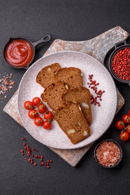 Koyu bir zeminde tohumlu, taneli, tuzlu ve baharatlı kahverengi ekmek.