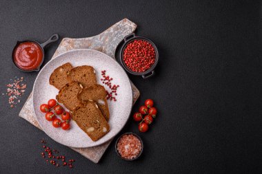 Koyu bir zeminde tohumlu, taneli, tuzlu ve baharatlı kahverengi ekmek.