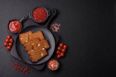 Koyu bir zeminde tohumlu, taneli, tuzlu ve baharatlı kahverengi ekmek.