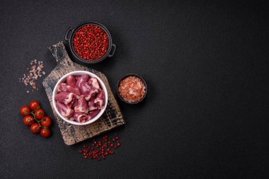 Raw chicken hearts with salt, spices and herbs on a dark concrete background clipart