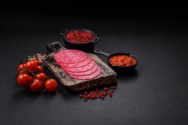 Lezzetli tütsülenmiş salam sosisi, tuz, baharat ve otlar koyu beton arka planda dilimler halinde kesilmiş.