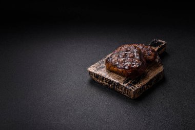 Izgarada pişirilmiş sulu biftek. Koyu beton arka planda tuz, baharat ve otlarla.