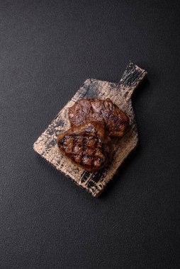 Izgarada pişirilmiş sulu biftek. Koyu beton arka planda tuz, baharat ve otlarla.