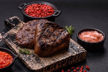 Izgarada pişirilmiş sulu biftek. Koyu beton arka planda tuz, baharat ve otlarla.