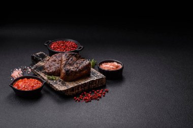 Izgarada pişirilmiş sulu biftek. Koyu beton arka planda tuz, baharat ve otlarla.