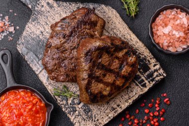 Izgarada pişirilmiş sulu biftek. Koyu beton arka planda tuz, baharat ve otlarla.