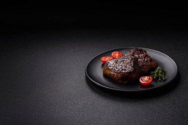 Izgarada pişirilmiş sulu biftek. Koyu beton arka planda tuz, baharat ve otlarla.