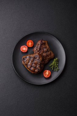 Izgarada pişirilmiş sulu biftek. Koyu beton arka planda tuz, baharat ve otlarla.