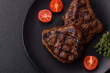 Izgarada pişirilmiş sulu biftek. Koyu beton arka planda tuz, baharat ve otlarla.