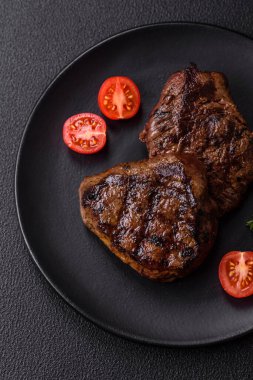 Izgarada pişirilmiş sulu biftek. Koyu beton arka planda tuz, baharat ve otlarla.