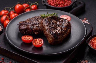 Izgarada pişirilmiş sulu biftek. Koyu beton arka planda tuz, baharat ve otlarla.