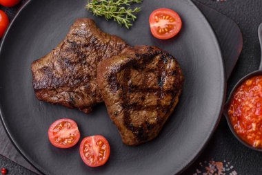 Izgarada pişirilmiş sulu biftek. Koyu beton arka planda tuz, baharat ve otlarla.