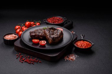 Izgarada pişirilmiş sulu biftek. Koyu beton arka planda tuz, baharat ve otlarla.