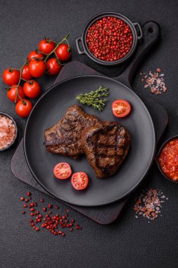 Izgarada pişirilmiş sulu biftek. Koyu beton arka planda tuz, baharat ve otlarla.
