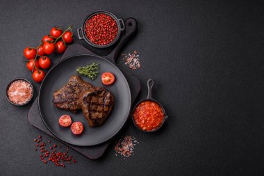 Izgarada pişirilmiş sulu biftek. Koyu beton arka planda tuz, baharat ve otlarla.