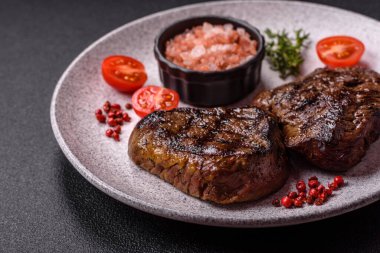 Izgarada pişirilmiş sulu biftek. Koyu beton arka planda tuz, baharat ve otlarla.