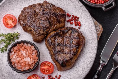 Izgarada pişirilmiş sulu biftek. Koyu beton arka planda tuz, baharat ve otlarla.