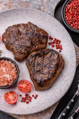 Izgarada pişirilmiş sulu biftek. Koyu beton arka planda tuz, baharat ve otlarla.