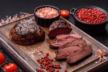 Izgarada pişirilmiş sulu biftek. Koyu beton arka planda tuz, baharat ve otlarla.