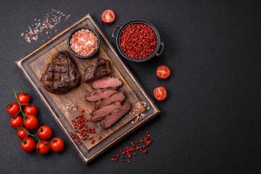 Izgarada pişirilmiş sulu biftek. Koyu beton arka planda tuz, baharat ve otlarla.