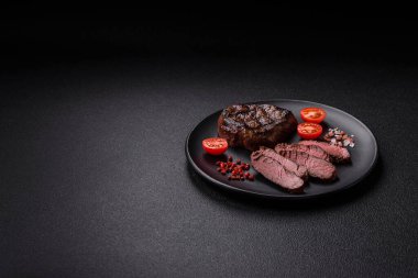 Izgarada pişirilmiş sulu biftek. Koyu beton arka planda tuz, baharat ve otlarla.