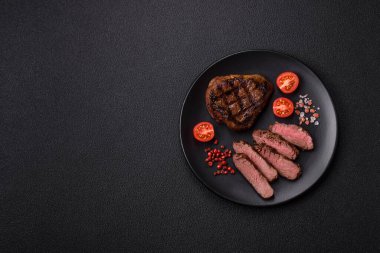 Izgarada pişirilmiş sulu biftek. Koyu beton arka planda tuz, baharat ve otlarla.