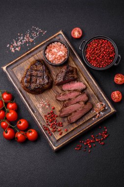 Izgarada pişirilmiş sulu biftek. Koyu beton arka planda tuz, baharat ve otlarla.