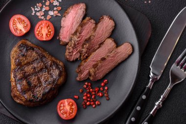 Izgarada pişirilmiş sulu biftek. Koyu beton arka planda tuz, baharat ve otlarla.