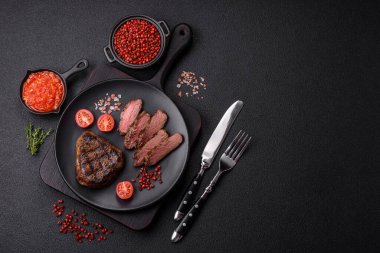 Izgarada pişirilmiş sulu biftek. Koyu beton arka planda tuz, baharat ve otlarla.