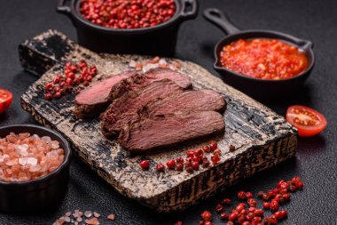 Izgarada pişirilmiş sulu biftek. Koyu beton arka planda tuz, baharat ve otlarla.