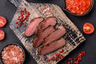 Izgarada pişirilmiş sulu biftek. Koyu beton arka planda tuz, baharat ve otlarla.