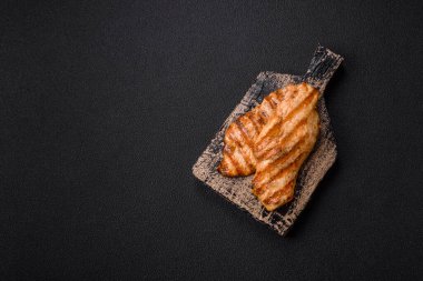 Izgarada pişirilmiş sulu tavuk filetosu. Koyu beton arka planda tuz, baharat ve otlarla birlikte.