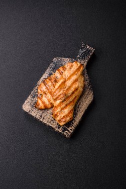 Izgarada pişirilmiş sulu tavuk filetosu. Koyu beton arka planda tuz, baharat ve otlarla birlikte.