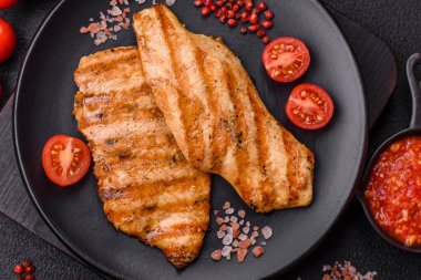 Izgarada pişirilmiş sulu tavuk filetosu. Koyu beton arka planda tuz, baharat ve otlarla birlikte.