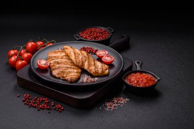 Izgarada pişirilmiş sulu tavuk filetosu. Koyu beton arka planda tuz, baharat ve otlarla birlikte.