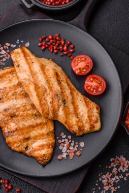 Izgarada pişirilmiş sulu tavuk filetosu. Koyu beton arka planda tuz, baharat ve otlarla birlikte.