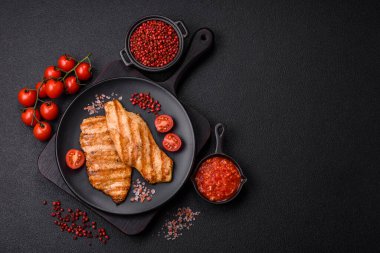 Izgarada pişirilmiş sulu tavuk filetosu. Koyu beton arka planda tuz, baharat ve otlarla birlikte.