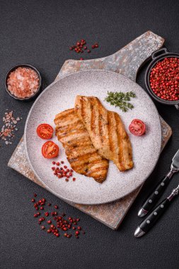 Izgarada pişirilmiş sulu tavuk filetosu. Koyu beton arka planda tuz, baharat ve otlarla birlikte.