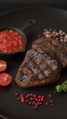 Izgarada pişirilmiş sulu biftek. Koyu beton arka planda tuz, baharat ve otlarla.