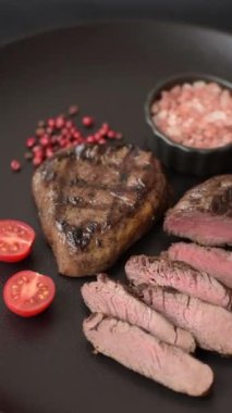 Izgarada pişirilmiş sulu biftek. Koyu beton arka planda tuz, baharat ve otlarla.