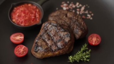 Izgarada pişirilmiş sulu biftek. Koyu beton arka planda tuz, baharat ve otlarla.