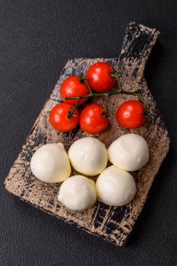 Lezzetli taze mozzarella peyniri domatesli, tuzlu ve baharatlı koyu beton arka planda.