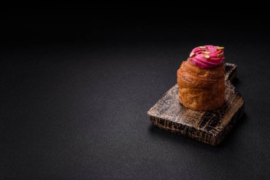 Sweet craffin or panettone garnished with raspberry and pistachio flavored cream on a dark concrete background clipart