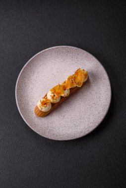 Tatlı eklerleri ya da çikolata dolgulu profiteroller ve koyu beton arka planda krema ve kurutulmuş portakallarla kaplı.