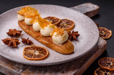 Tatlı eklerleri ya da çikolata dolgulu profiteroller ve koyu beton arka planda krema ve kurutulmuş portakallarla kaplı.