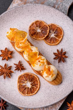 Tatlı eklerleri ya da çikolata dolgulu profiteroller ve koyu beton arka planda krema ve kurutulmuş portakallarla kaplı.