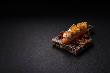 Tatlı eklerleri ya da çikolata dolgulu profiteroller ve koyu beton arka planda krema ve kurutulmuş portakallarla kaplı.