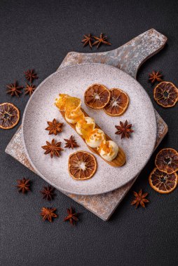 Tatlı eklerleri ya da çikolata dolgulu profiteroller ve koyu beton arka planda krema ve kurutulmuş portakallarla kaplı.