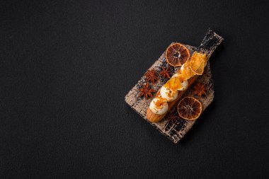 Tatlı eklerleri ya da çikolata dolgulu profiteroller ve koyu beton arka planda krema ve kurutulmuş portakallarla kaplı.