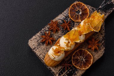 Tatlı eklerleri ya da çikolata dolgulu profiteroller ve koyu beton arka planda krema ve kurutulmuş portakallarla kaplı.